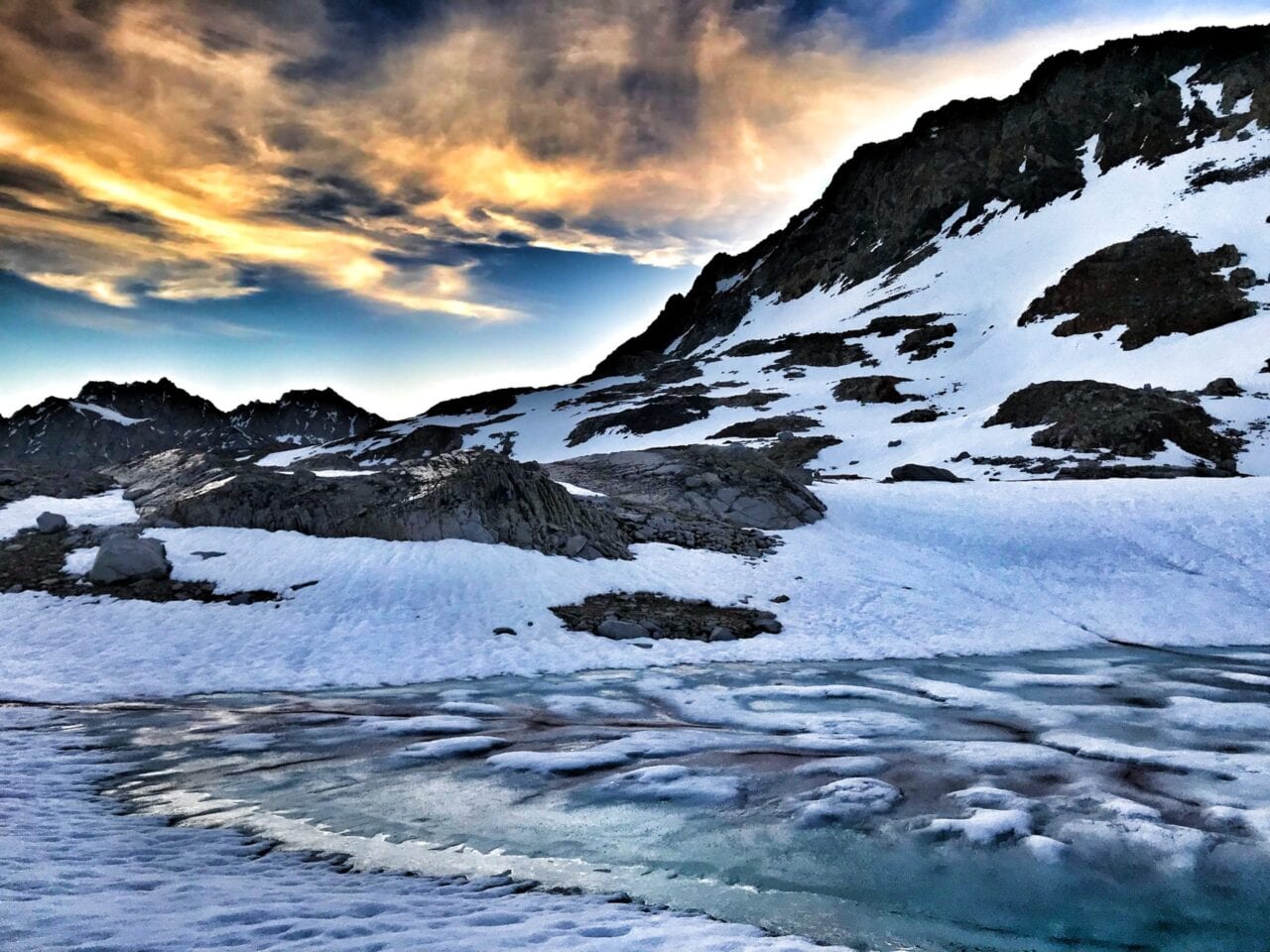 A beautiful view of a sunset over a snow covered mountain with a lake.