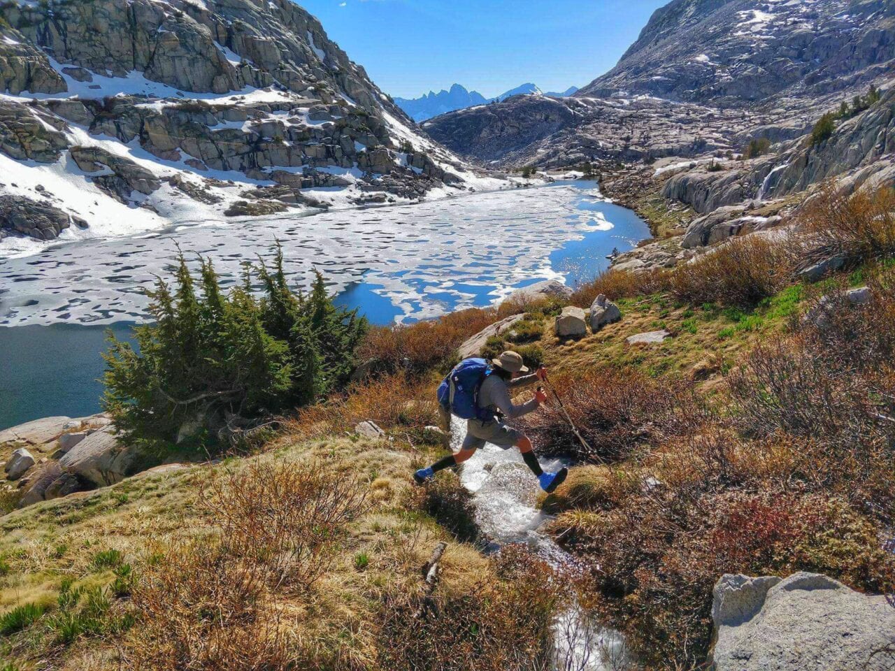 A man standing over a trail with his backpack on.