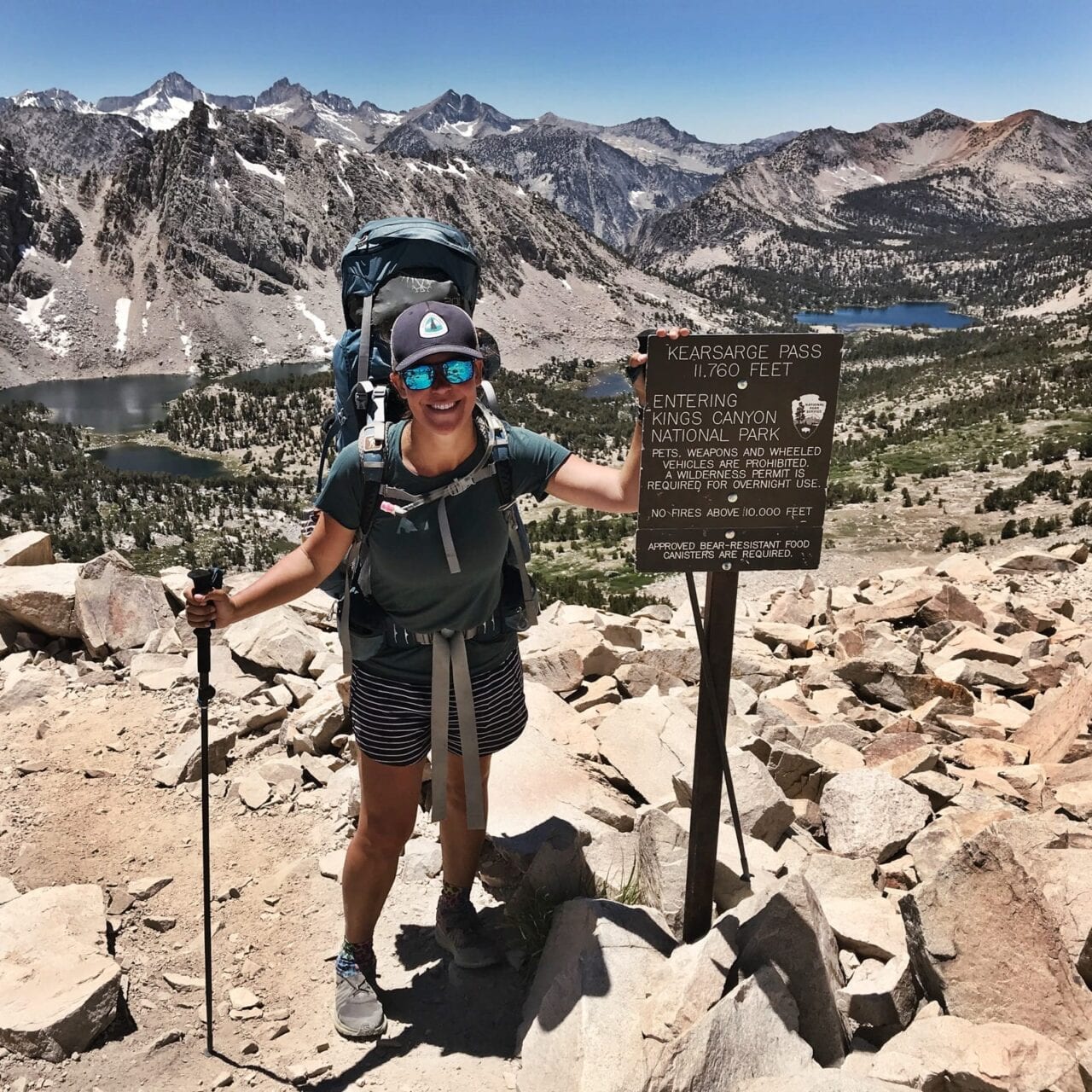 A woman hiker standing next to a trail sign.