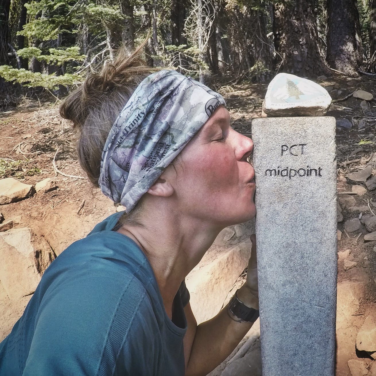 A woman hiker kissing a Pacific Crest Trail sign post.
