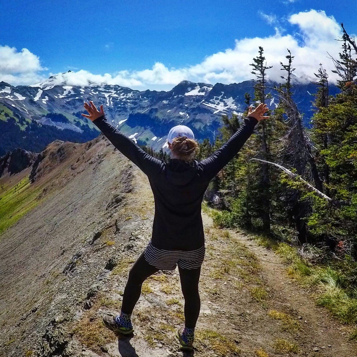 A woman hiker standing with her arms up in the air while looking out at the mountains.