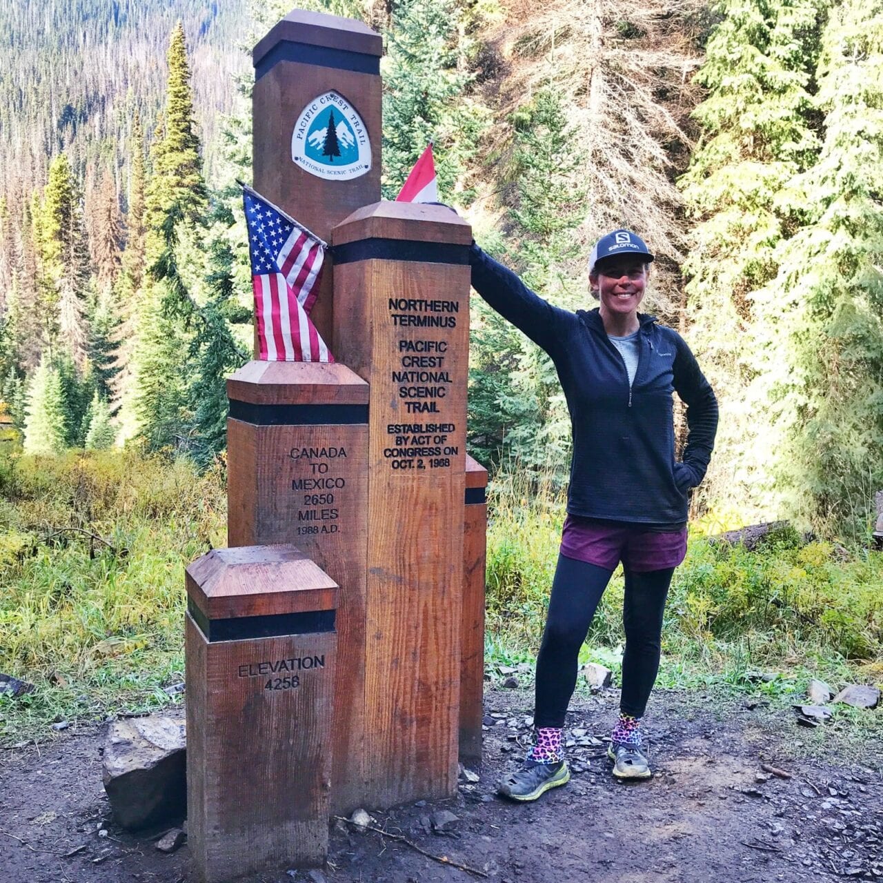 A woman hiker standing next to the northern terminus on the Pacific Crest Trail.