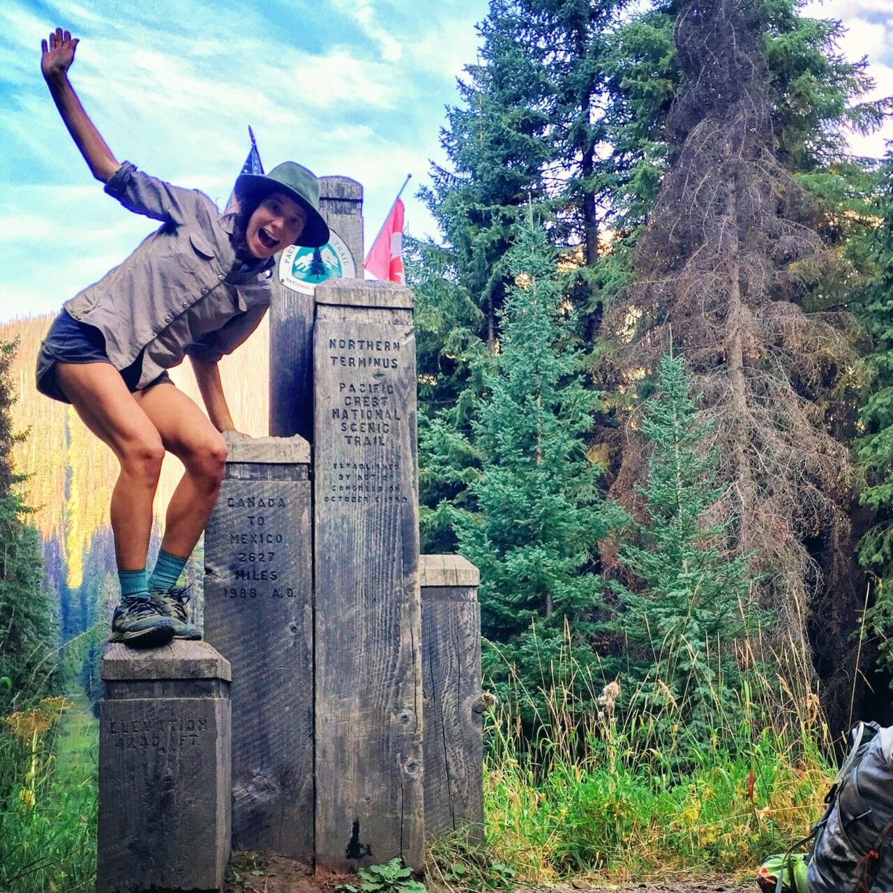 A woman hiker stands on the northern terminus of the Pacific Crest Trail.