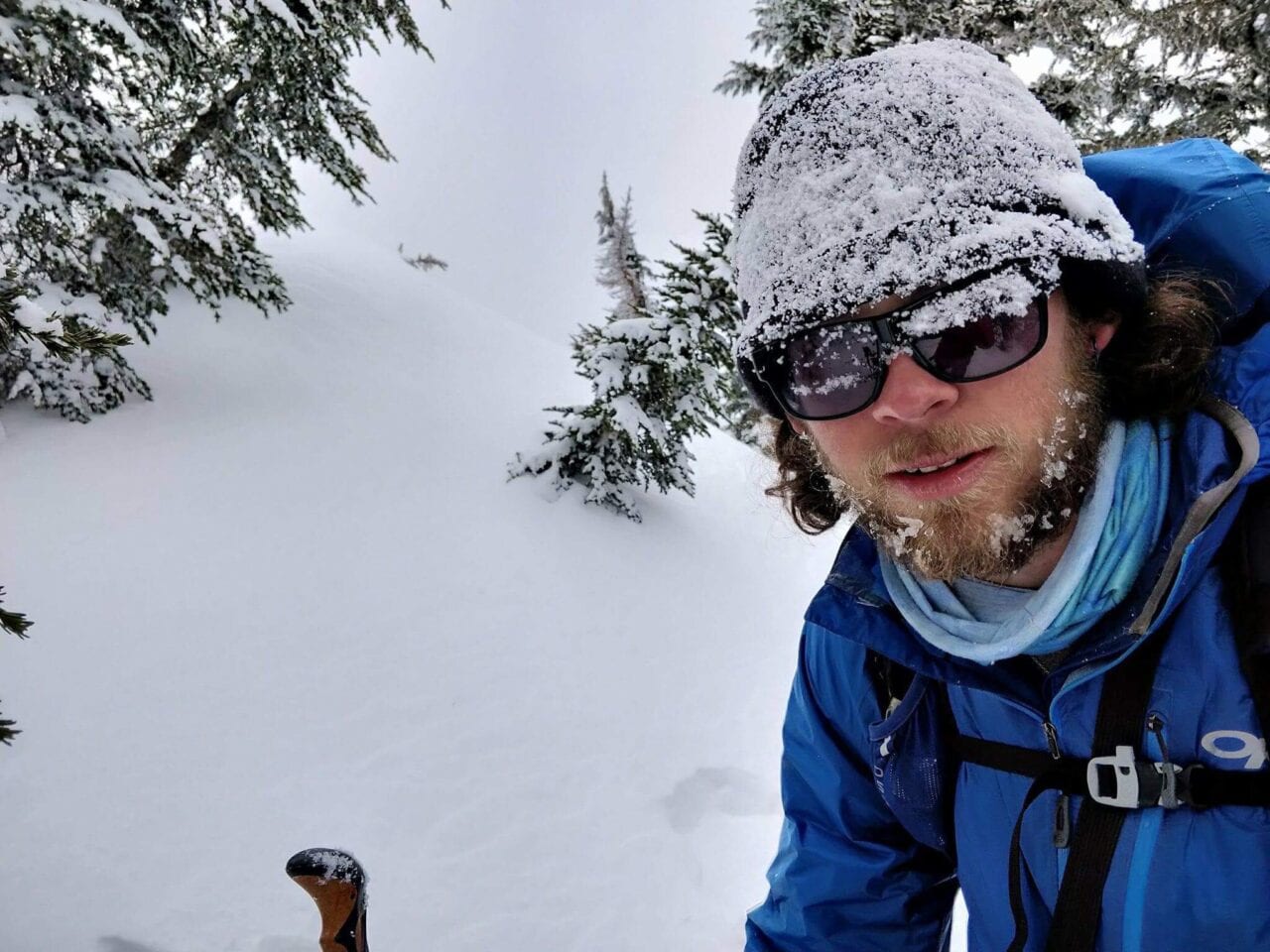 A hiker in the snow with a beanie and sunglasses on.