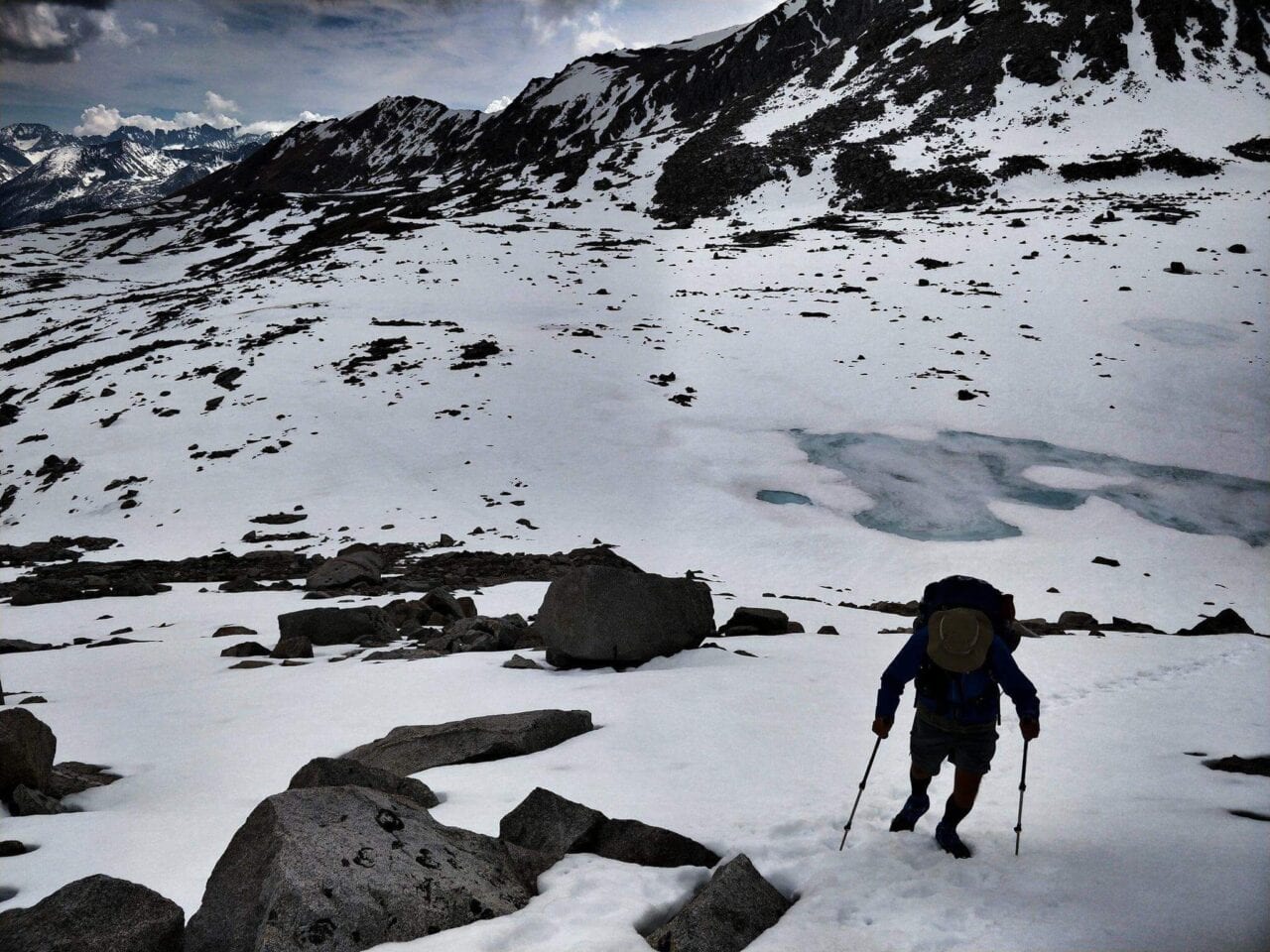 A hiker hiking up a snow covered mountain holding trekking poles.