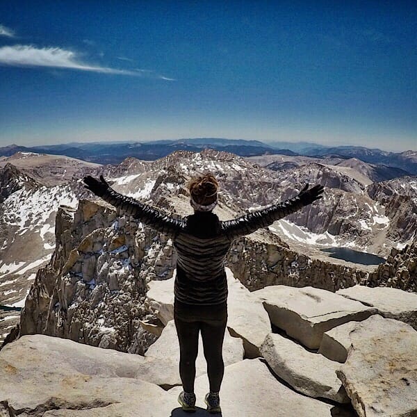 A woman hiker standing with her arms up in the air looking at the mountains.