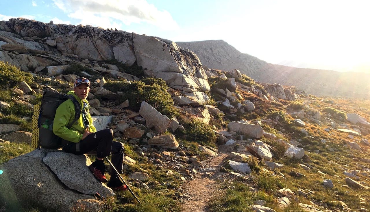 A hiker sitting on a rock with the sunset in the background.