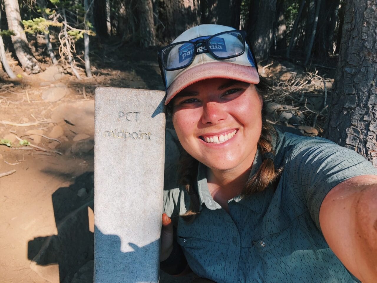 A woman hiker smiling next to a PCT trail sign post.