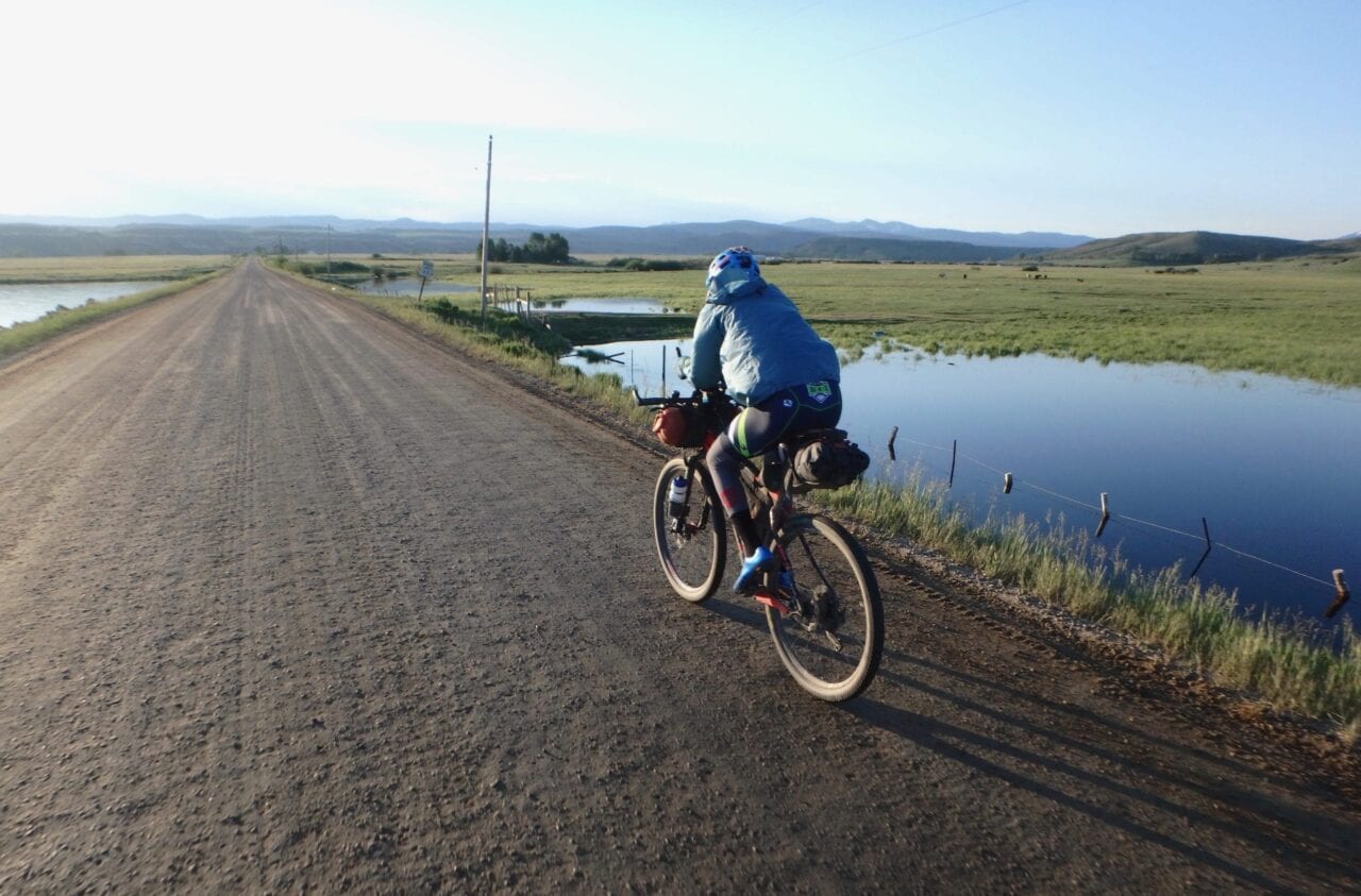 A man riding a bike on a road with a pond off to the side.