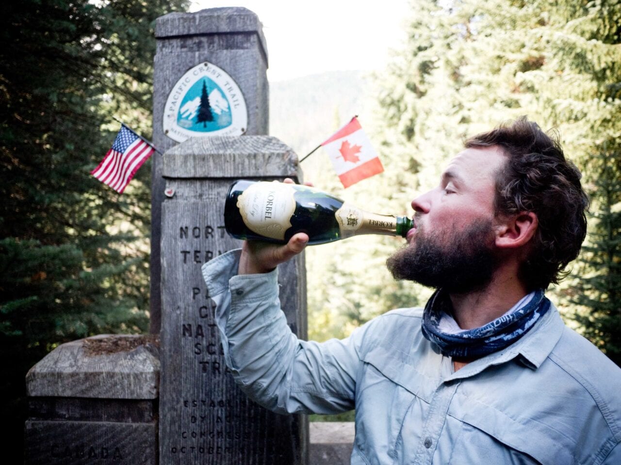 A man drinks out of a champagne bottle at the northern Pacific Crest Trail terminus.
