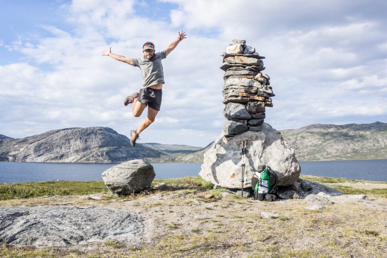 A man jumping in the air off a rock next to a lake.