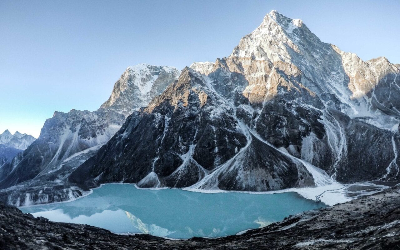 A beautiful snow covered mountain with a blue lake at the base.