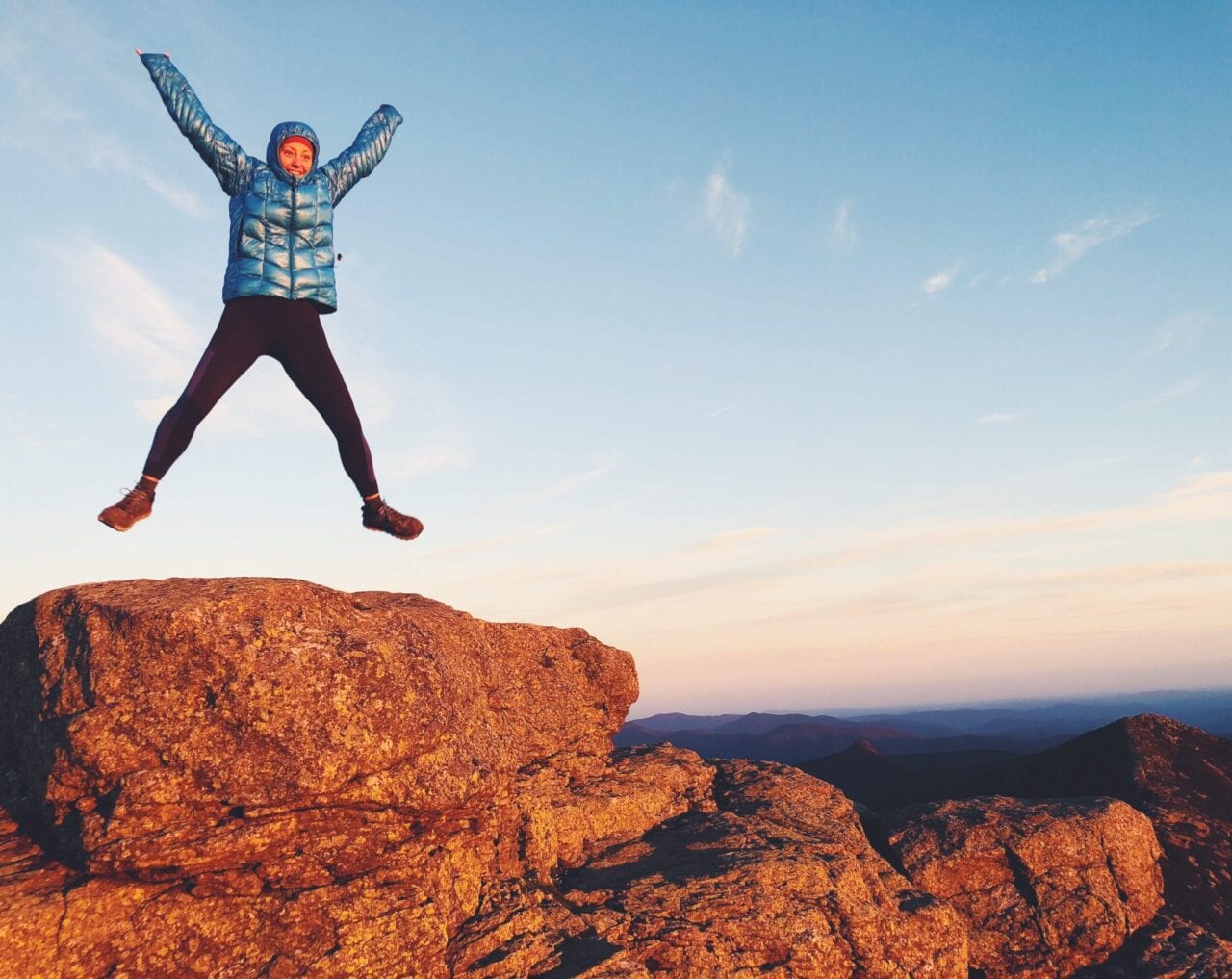 A woman jumping on a rock with her legs and arms out.