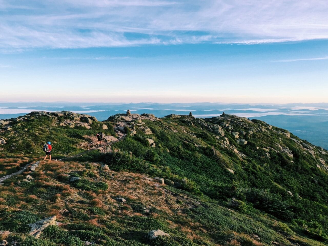 A beautiful view of a green mountain hill with hikers on the trail.