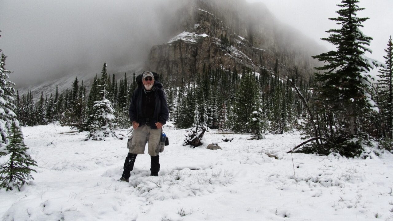 A man standing in the snow with a mountain and trees in the background.