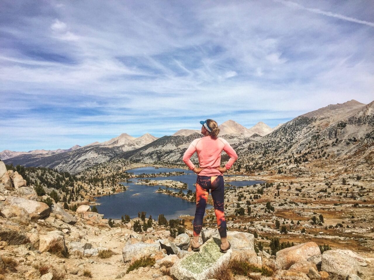 A woman standing on a hill overlooking a lake in the distance.