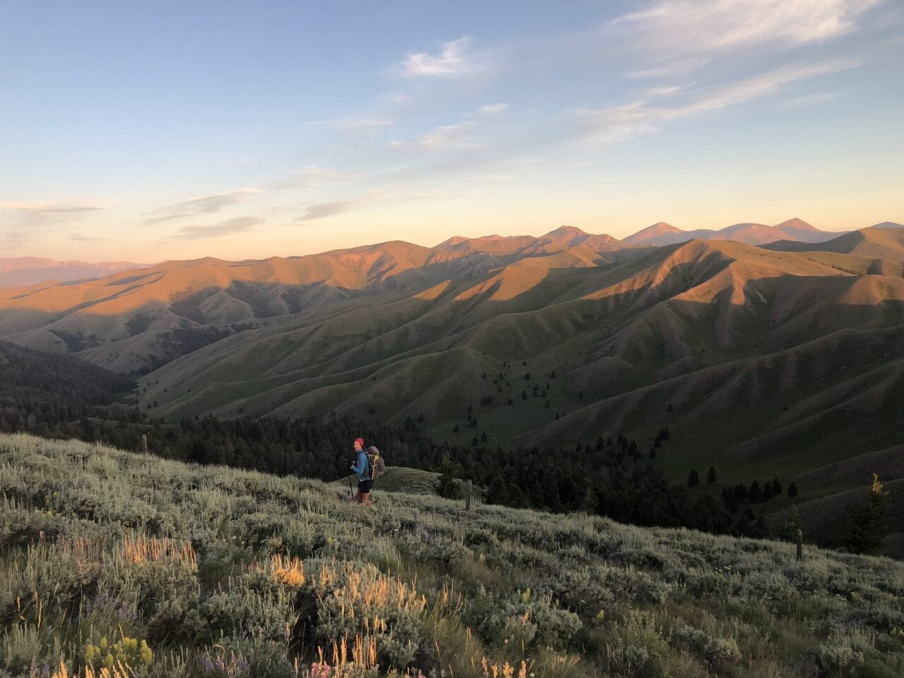 A woman hiking on a hill side with large mountains in the background.