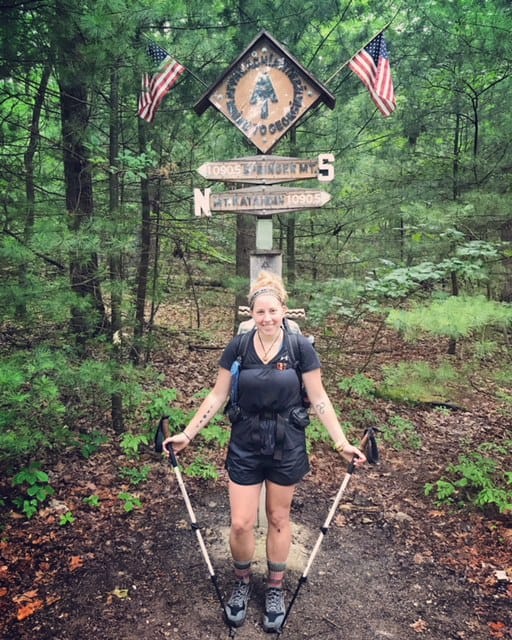 A hiker stands next to an Appalachian Trail sign