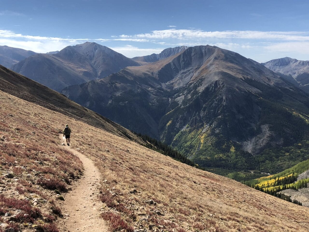 A hiker on a trail with big mountains in the distance.