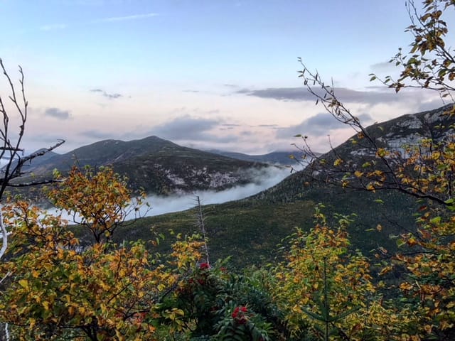 A view of the clouds in the mountains with fall colored trees.