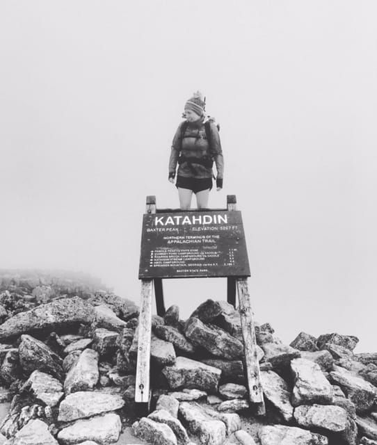 A hiker stands on top of the Mount Katahdin trail sign.