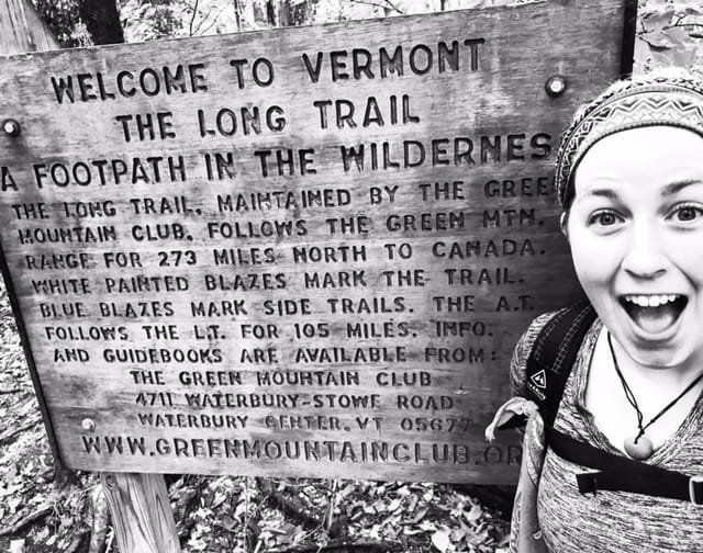 A woman smiles next to a Long Trail sign.