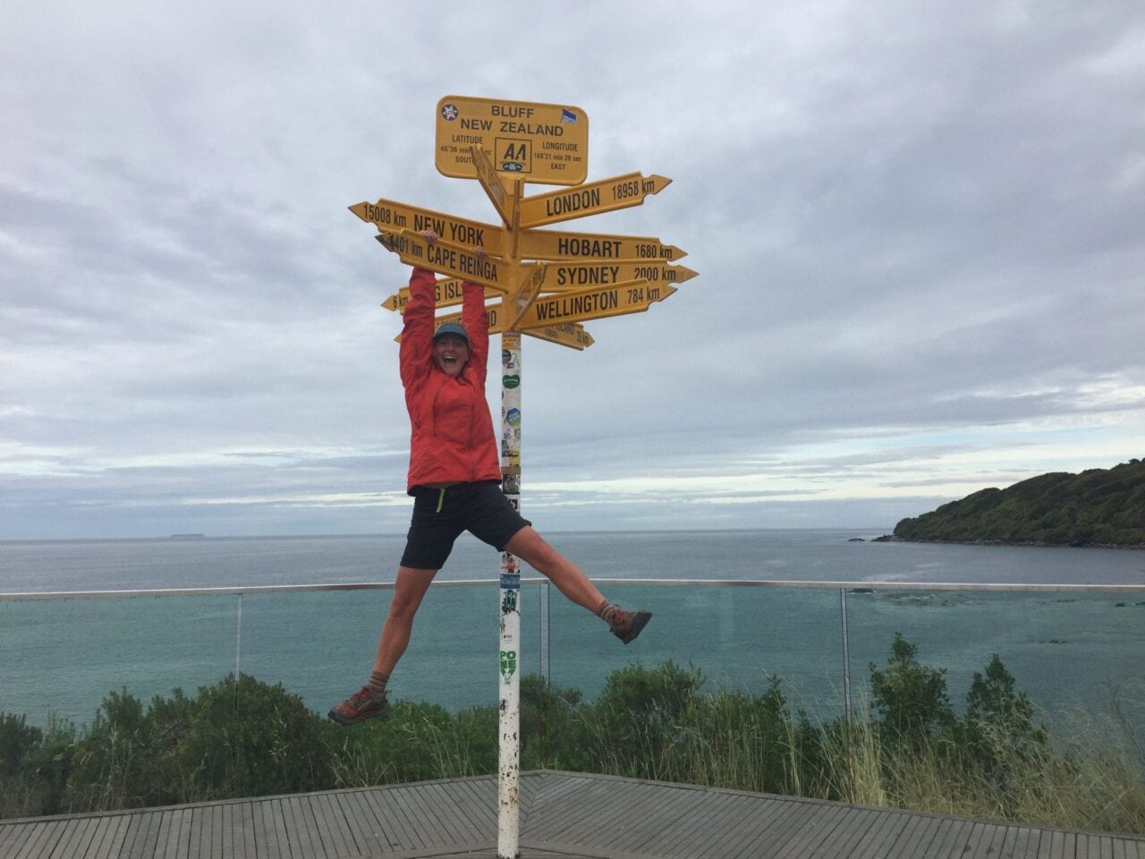 A woman hanging on the Te Araroa starting sign.