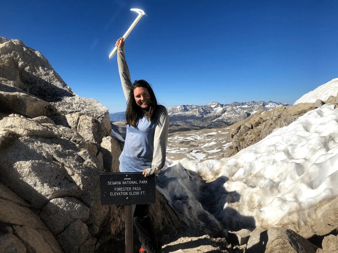 A woman holding an ice pick in the air next to the Sequoia National Park sign.