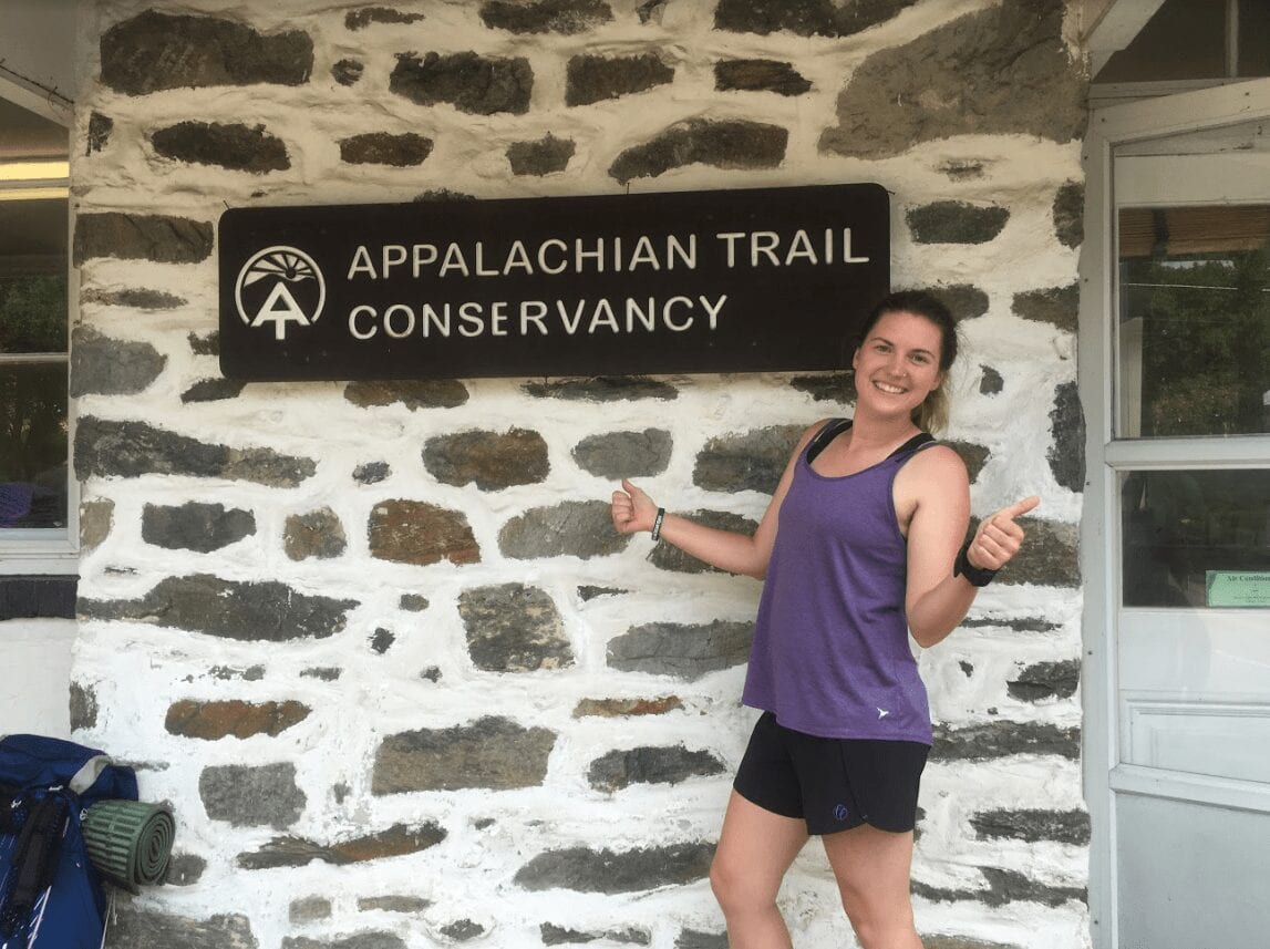 A woman stands with her thumbs up next to the Appalachian Trail Conservancy sign.
