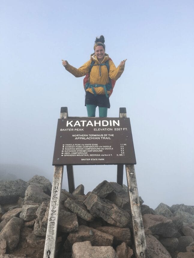 A woman standing on the Mount Katahdin sign.