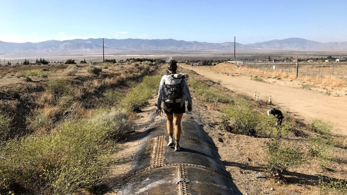 A hiker stands on an aquaduct pipe in the desert.