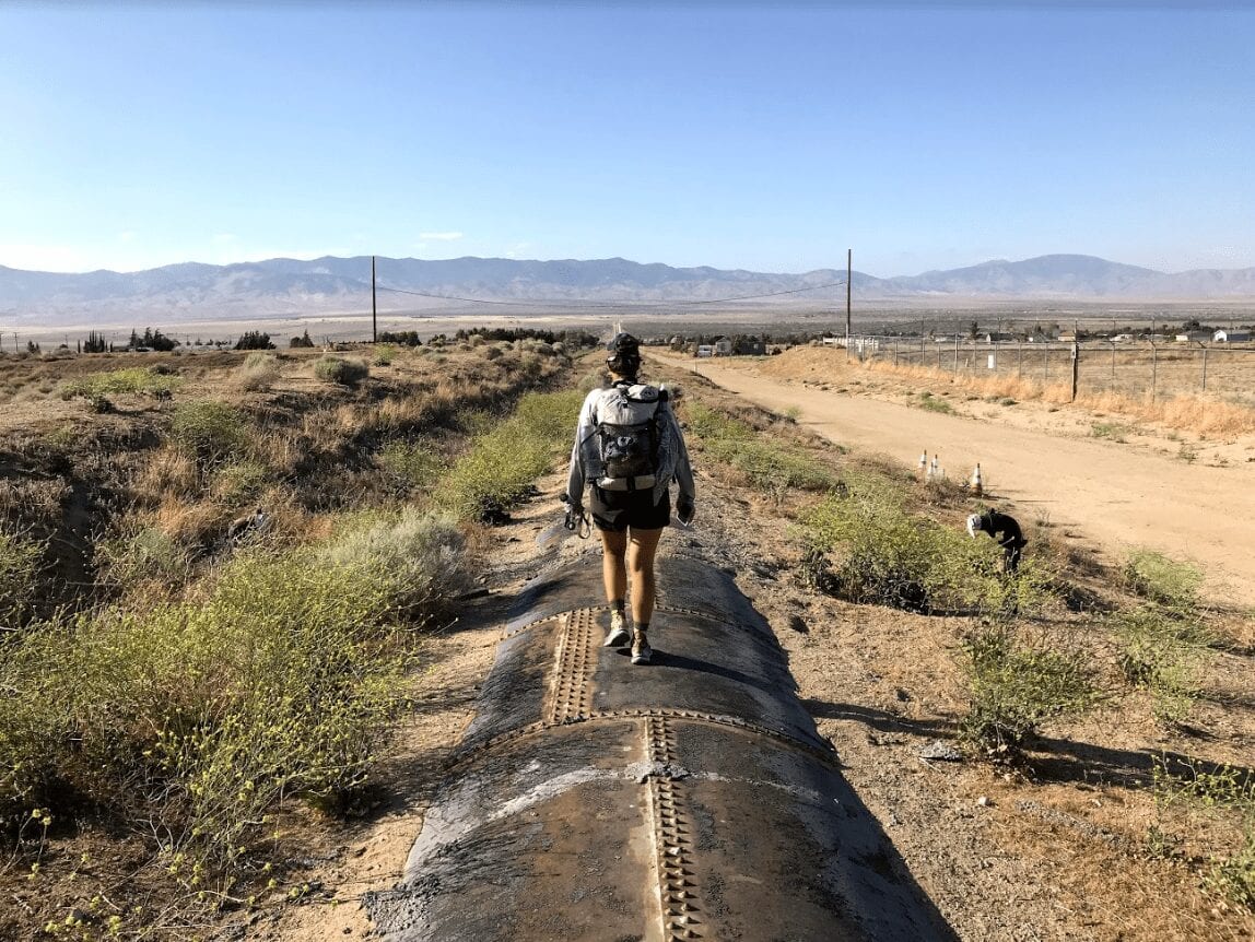 A hiker stands on an aquaduct pipe in the desert.