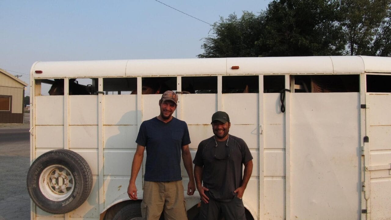 Two men standing in front of a horse trailer.