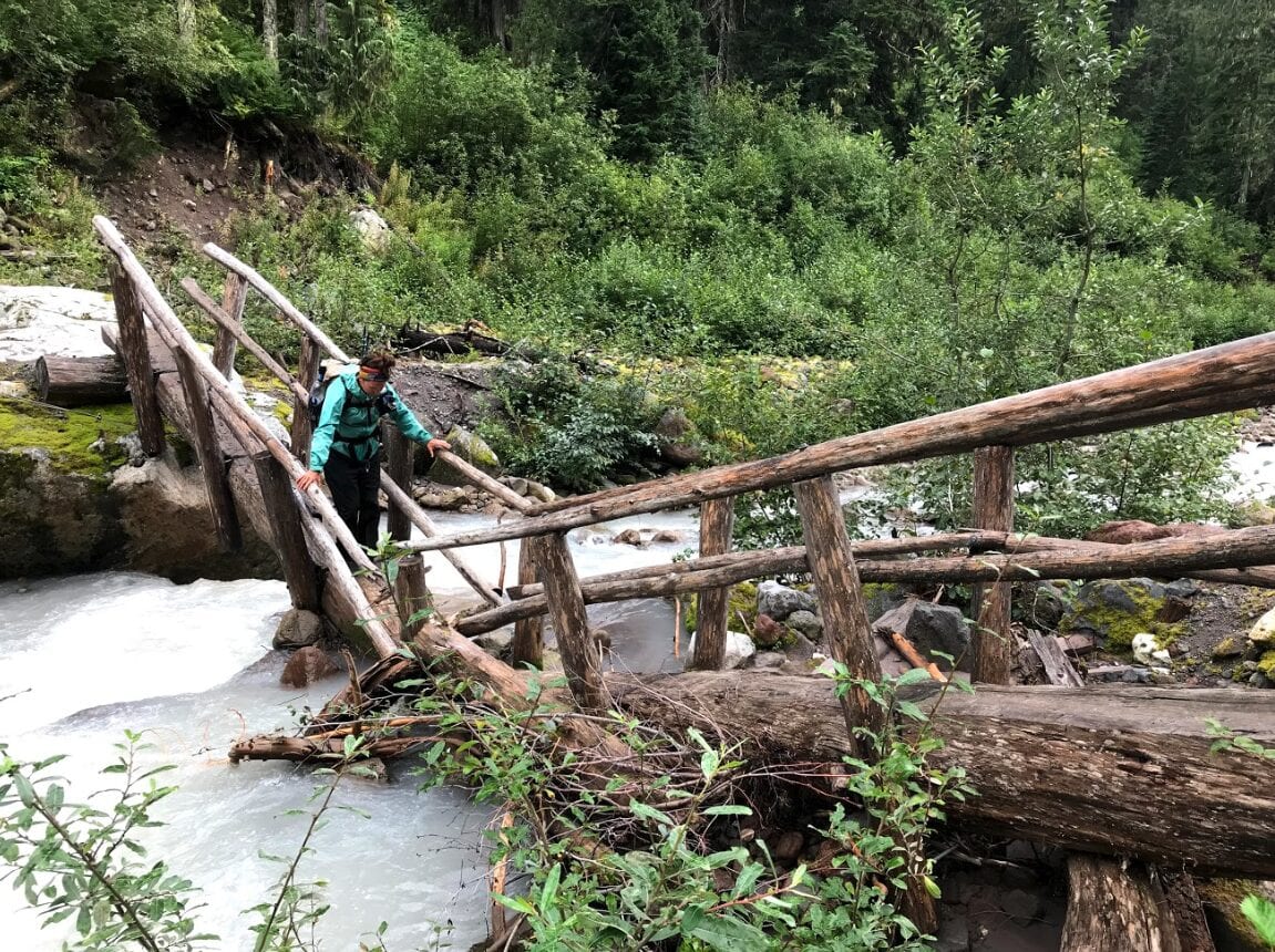 A woman crossing a river on a sketchy wooden tree bridge.