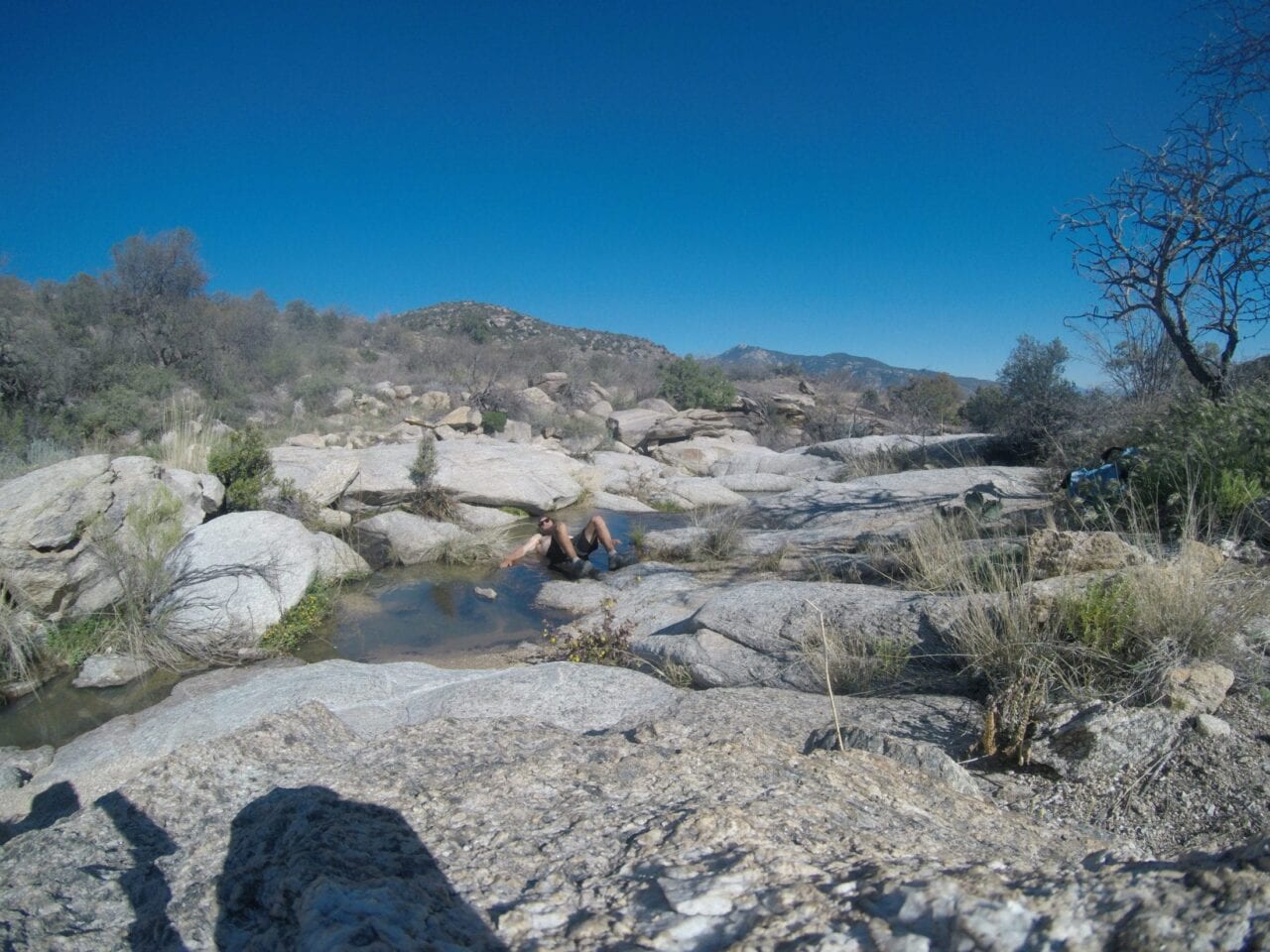A hiker laying down in a small pool of water in the desert rocks.