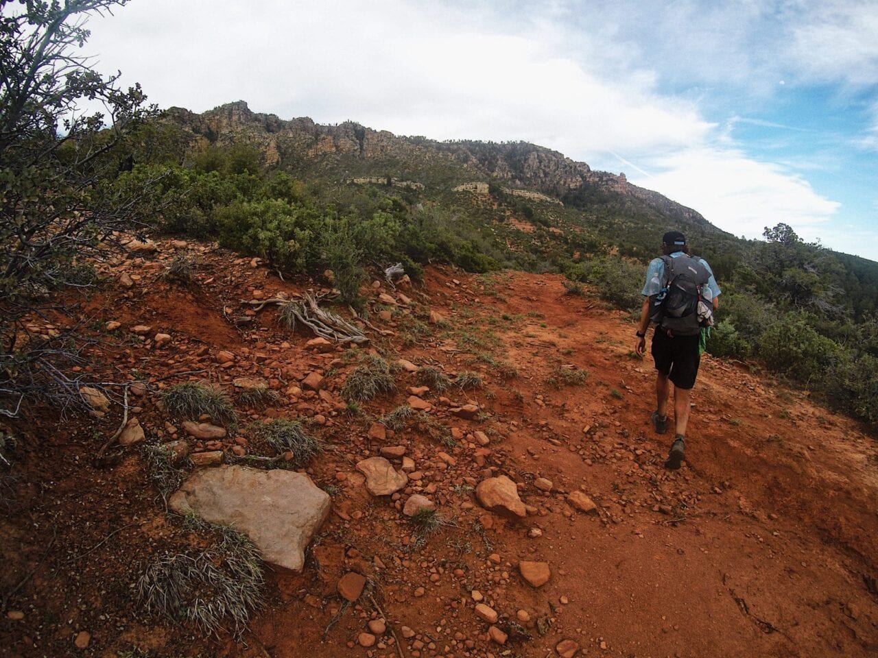 A hiker walking on a red dirt hill.