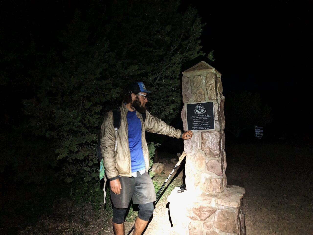 A hiker stands next to the northern terminus of the Arizona Trail at night.