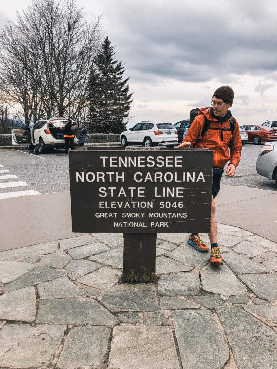 A hiker standing next to the Tennessee and North Carolina State Line sign on the Appalachian Trail.