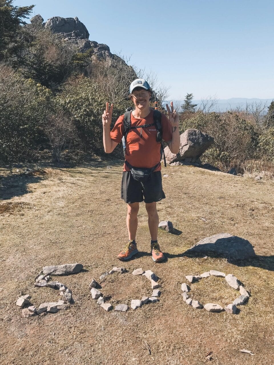 A hiker standing next to the number 500 made of rocks on the ground.