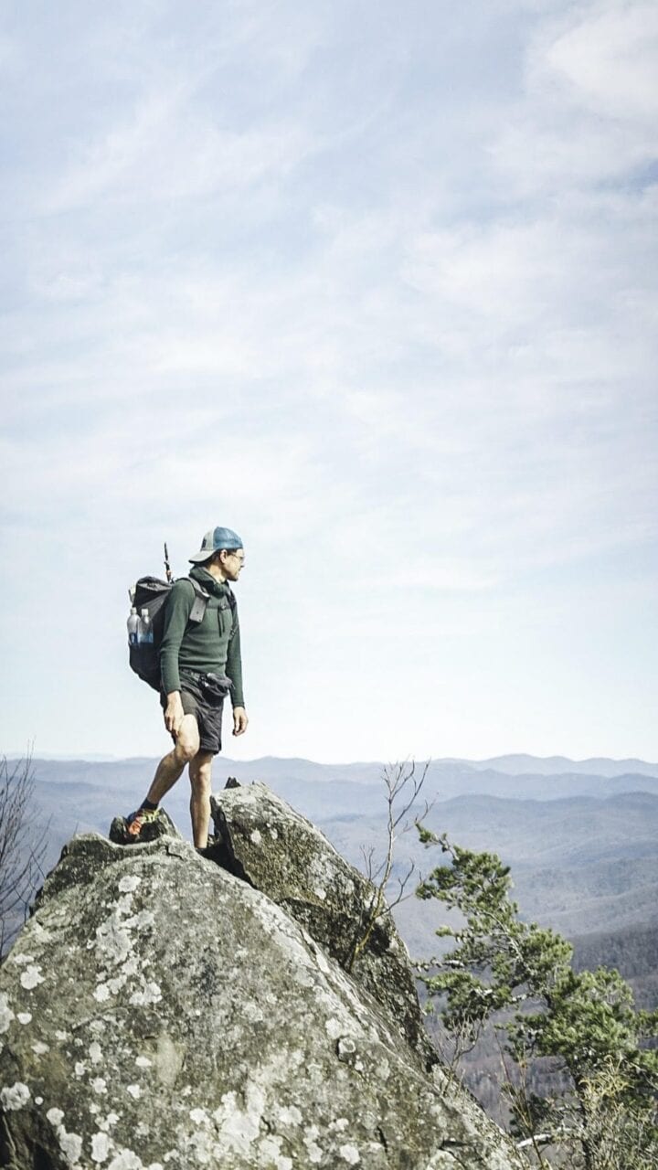 A hiker standing on a big boulder looking out at the scenery.