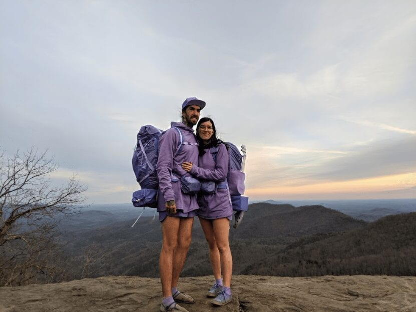 Two hikers in all purple clothes and gear hugging.