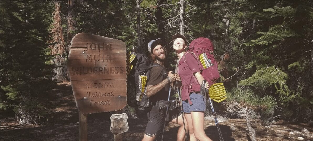 Two hikers pose in front of a John Muir Wilderness sign.
