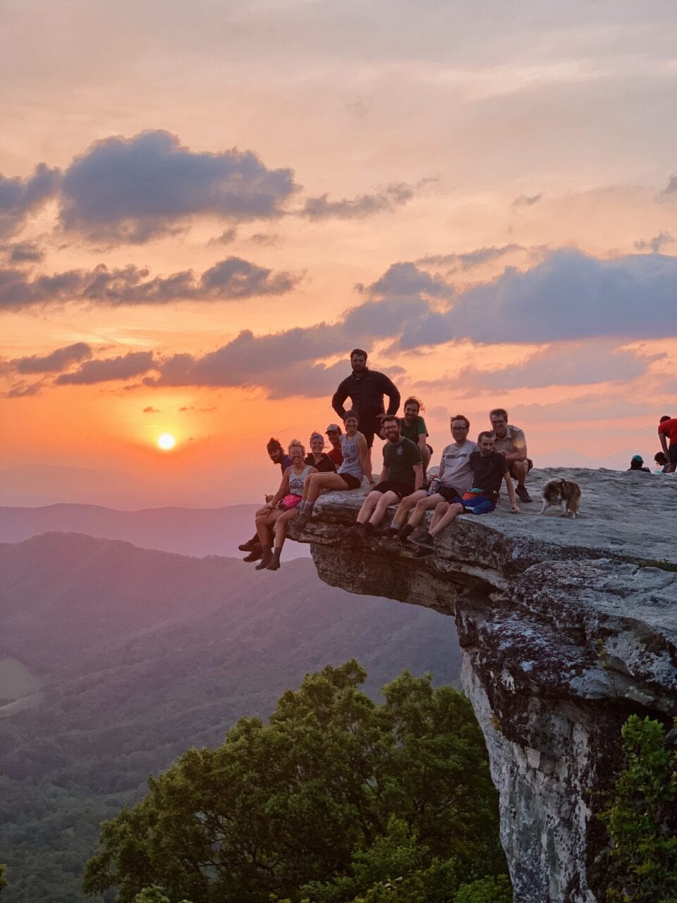 A group of hiker sit on a rock looking at the sunrise.