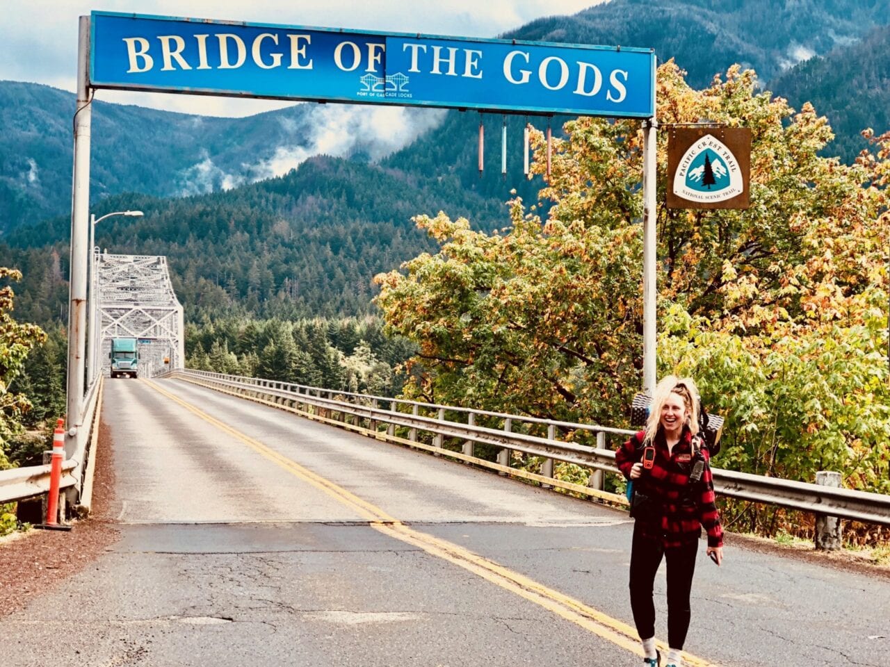 A woman standing in front of the Bridge of Gods sign.