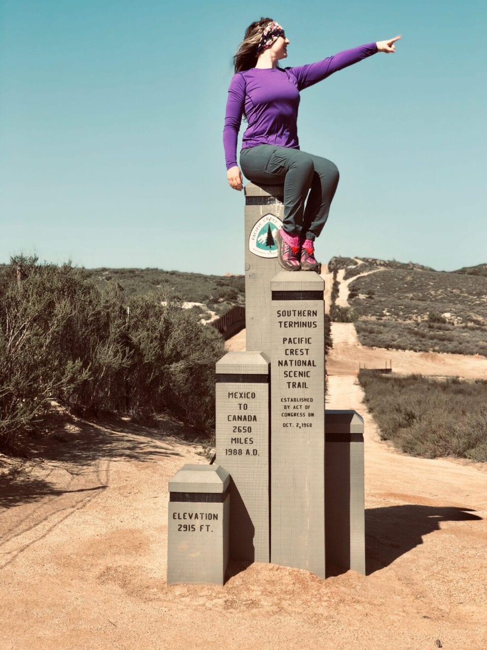 A woman sits on top of the southern terminus of the Pacific Crest Trail.
