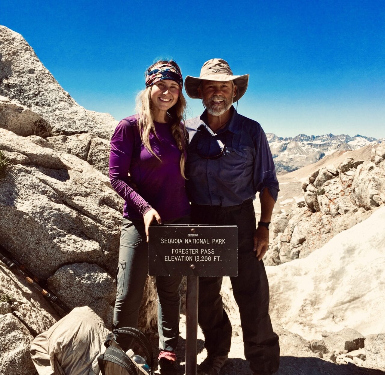 A man and woman stand behind the Forester Pass sign.