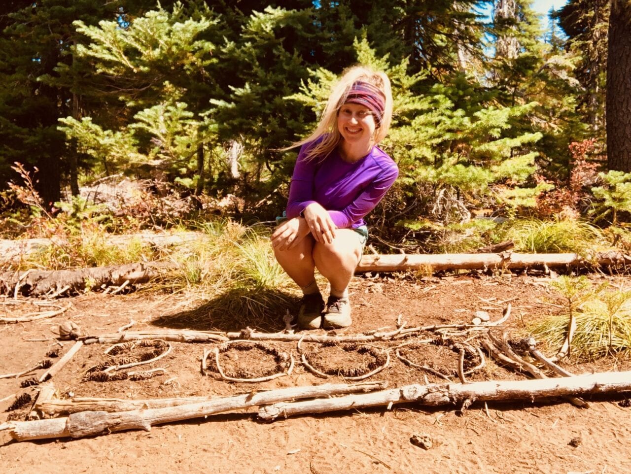 A woman squatting next to 2,000 out of sticks on the ground.