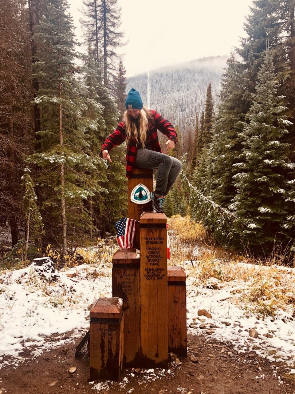 A woman sitting on top of the northern terminus of the Pacific Crest Trail.