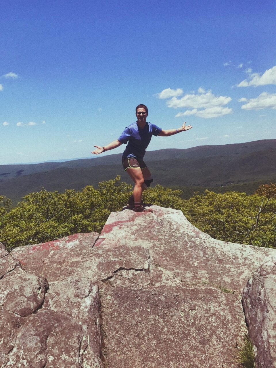 A hiker standing on a rock with her arms out.