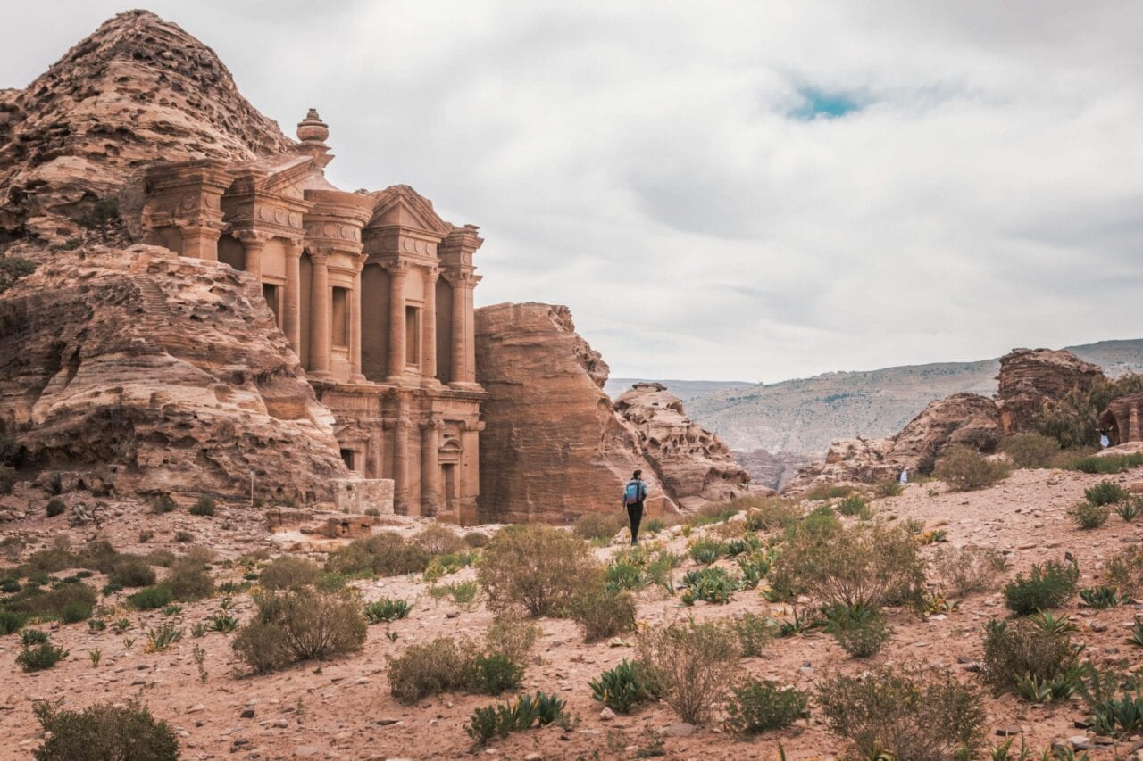 A hiker stands in front of Al Der Petra in a desert landscape.